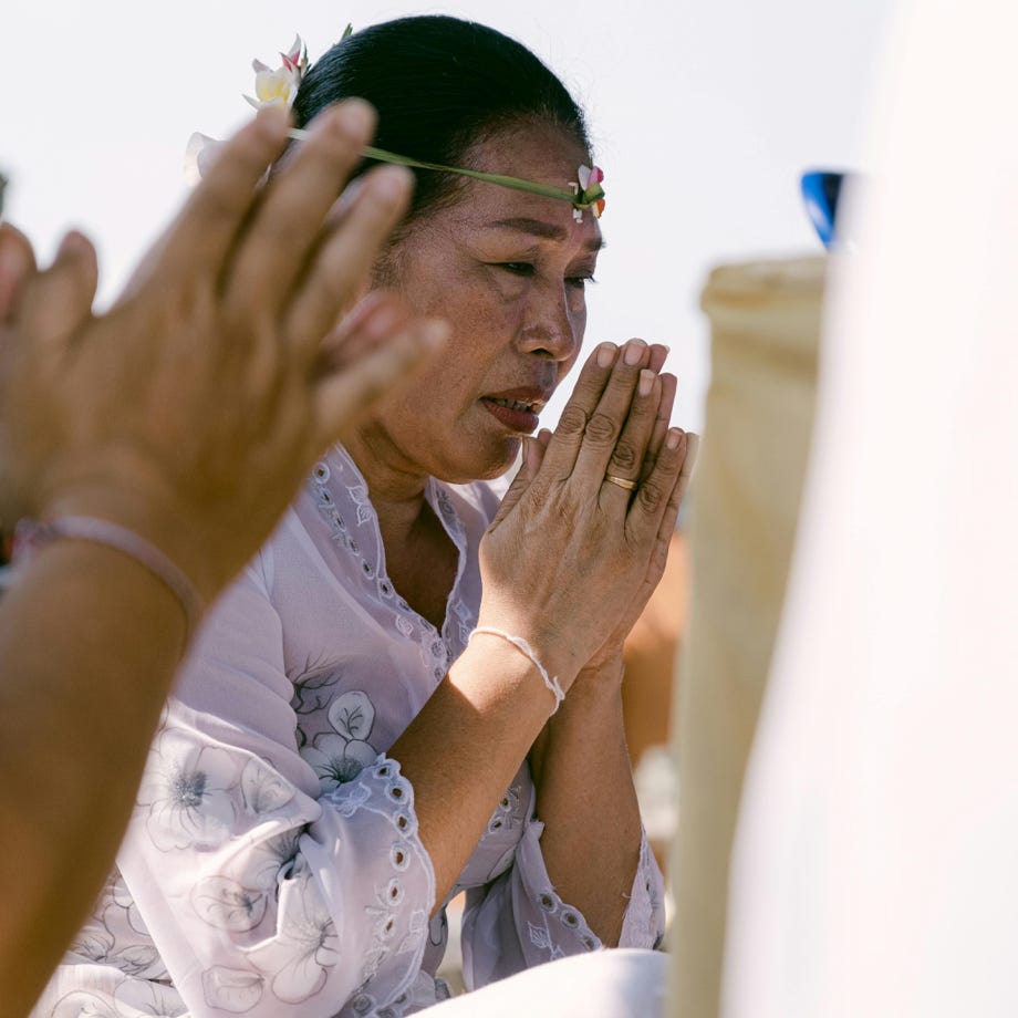 Une femme participe à une cérémonie culturelle, priant avec les mains jointes à l'extérieur.